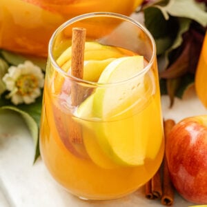 Apple Cider Sangria in a glass with fruit, flowers and leaves around it