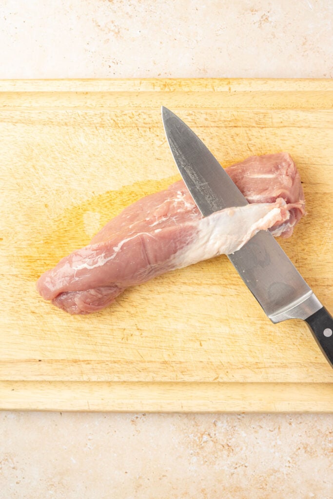 Knife, cutting off a silver skin on a pork tenderloin on a cutting board