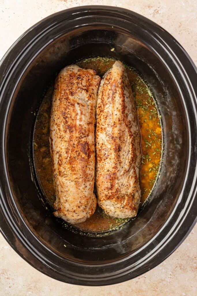 Slow cooker filled with Dijon mustard sauce, and seared pork tenderloins