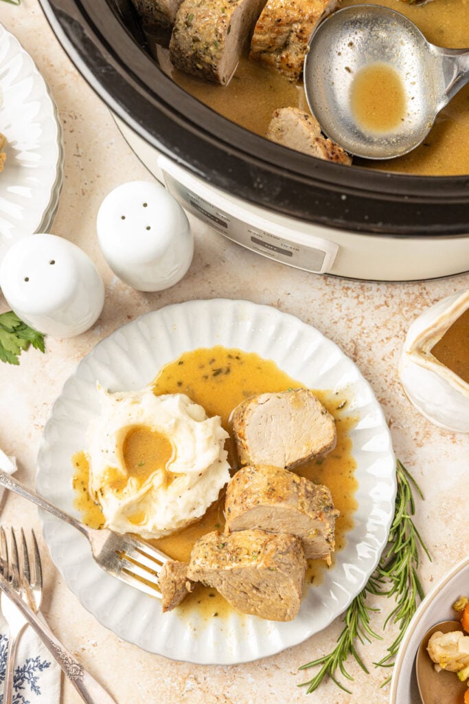 Slow Cooker Pork Tenderloin with Maple Dijon Sauce on a plate with mashed potatoes and slow cooker with the prok in the background.
