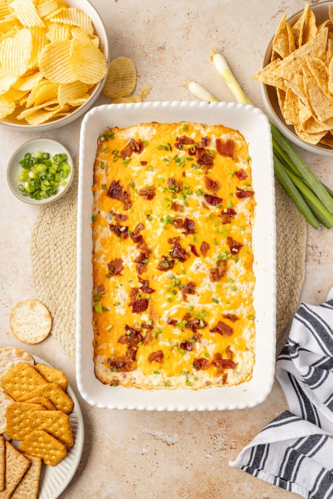 Cracked chicken dip in a 9 x 13 casserole pan with chips, crackers, and tortillas chips on the side