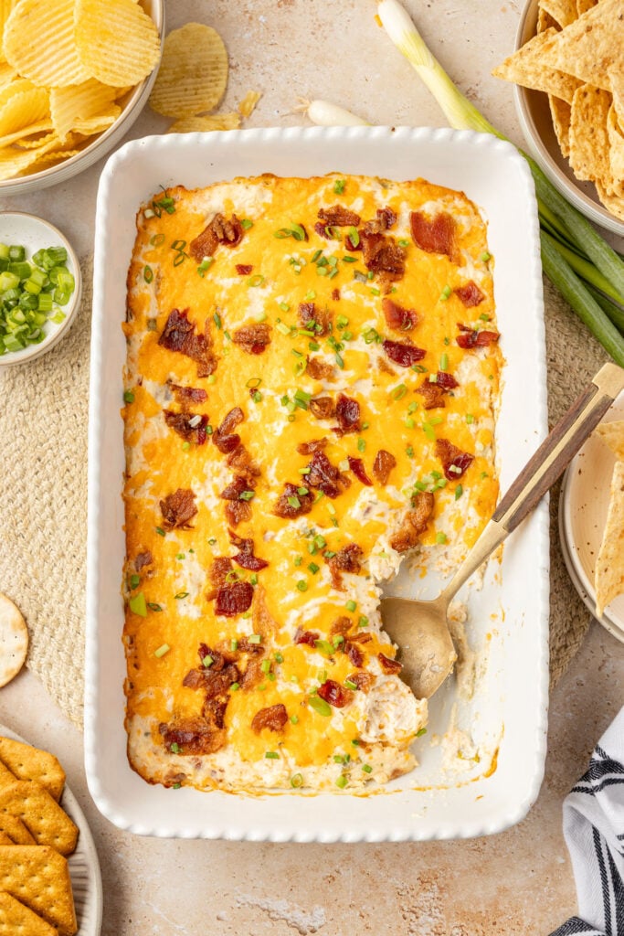 Cracked chicken dip in a 9 x 13 casserole pan with chips, crackers, and tortillas chips on the side