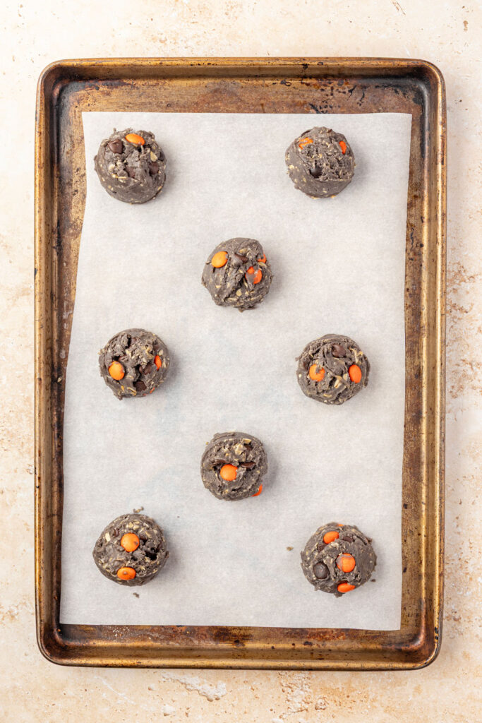 Raw Halloween Monster Cookies on a cookie sheet with parchment paper.