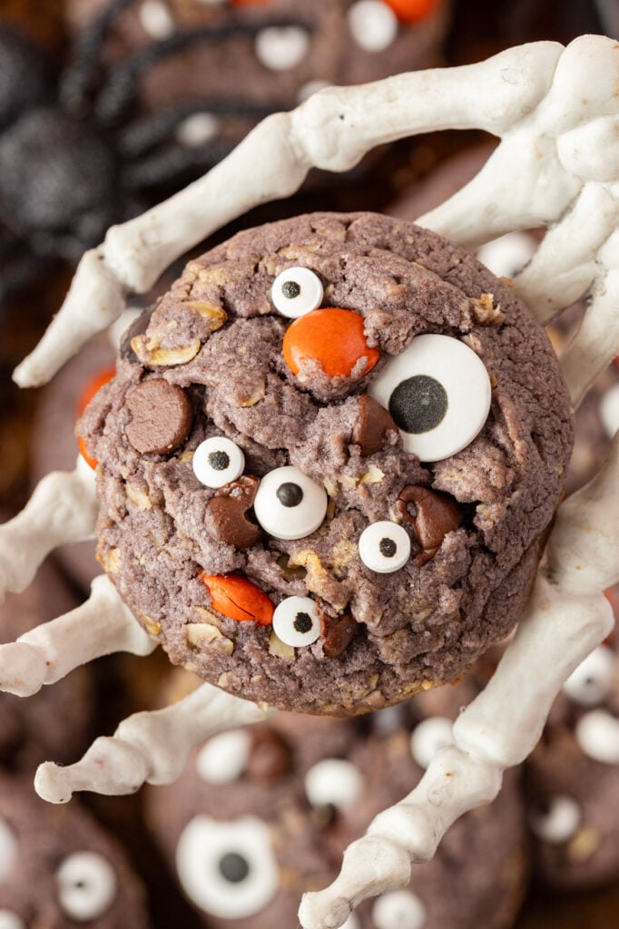 Skeleton holding a Halloween monster cookie in its hand up close.