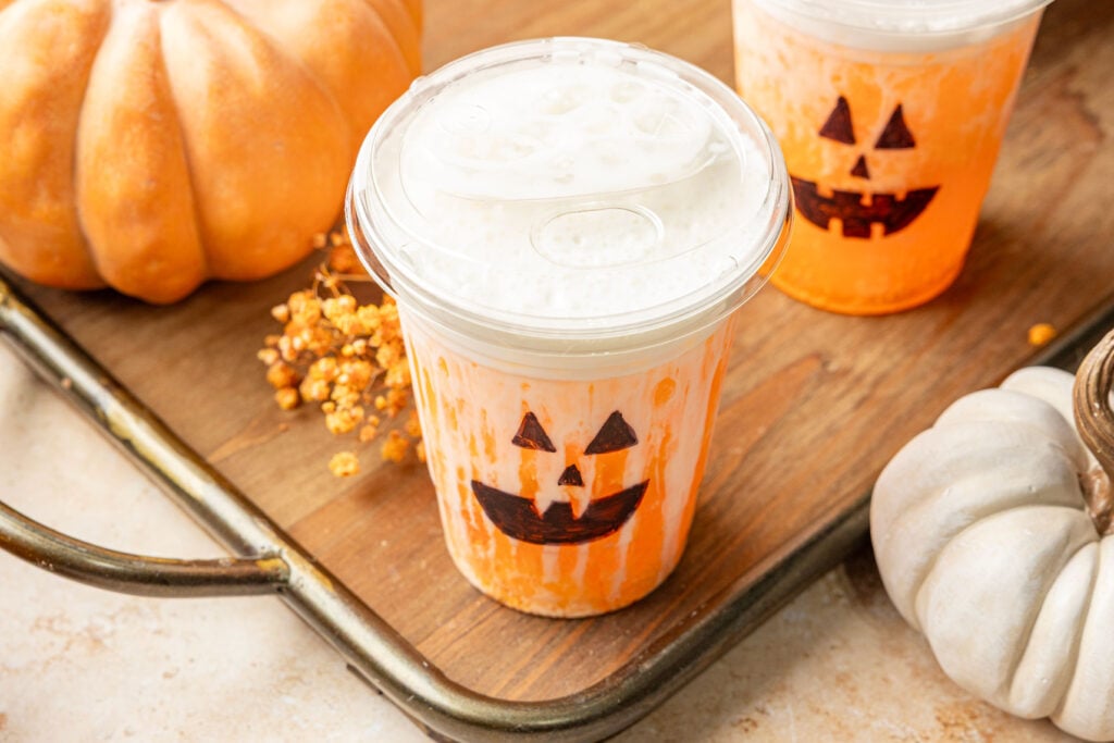 Jack-O’-Lantern Dirty Soda in a cup on a tray with pumpkins.