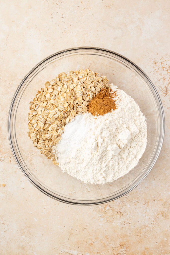 Flower, baking soda, baking powder, cinnamon, and oats in a mixing bowl.