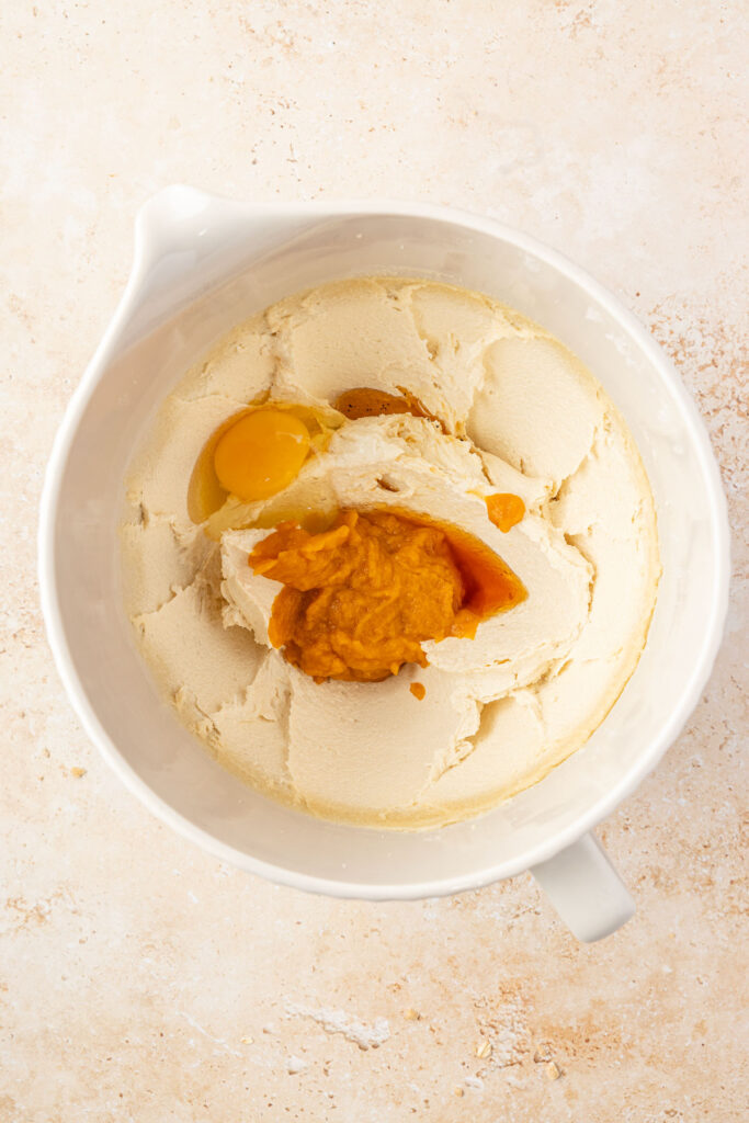Creamed butter and sugar in a mixing bowl with pumpkin purée, vanilla, an egg