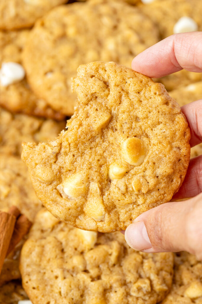 Hand holding a pumpkin oatmeal cookie with one bite taken out of it.