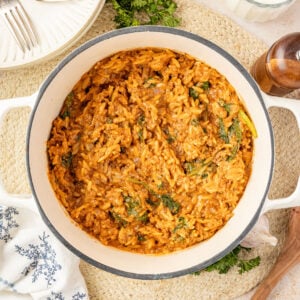 One Pot Beef Orzo in a Dutch oven on a placemat with plates and fresh herbs around it.