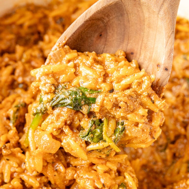 A wooden spoon scooping One Pot Beef Orzo from a white Dutch oven.