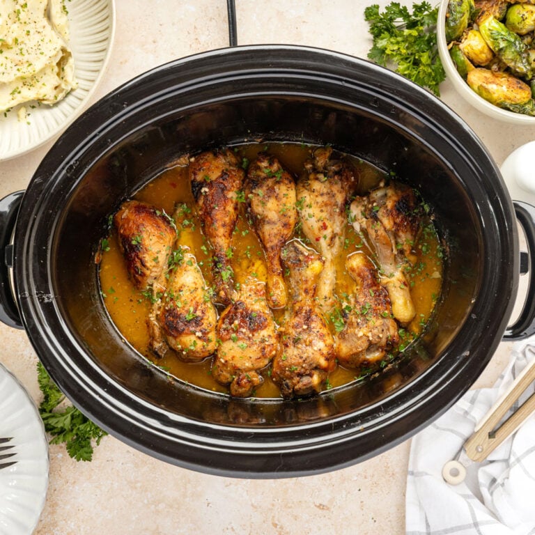 Slow cooker filled with finished slow cooker, chicken drumsticks.