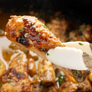 Tongues holding a piece of slow cooker, chicken drumsticks above the slow cooker.