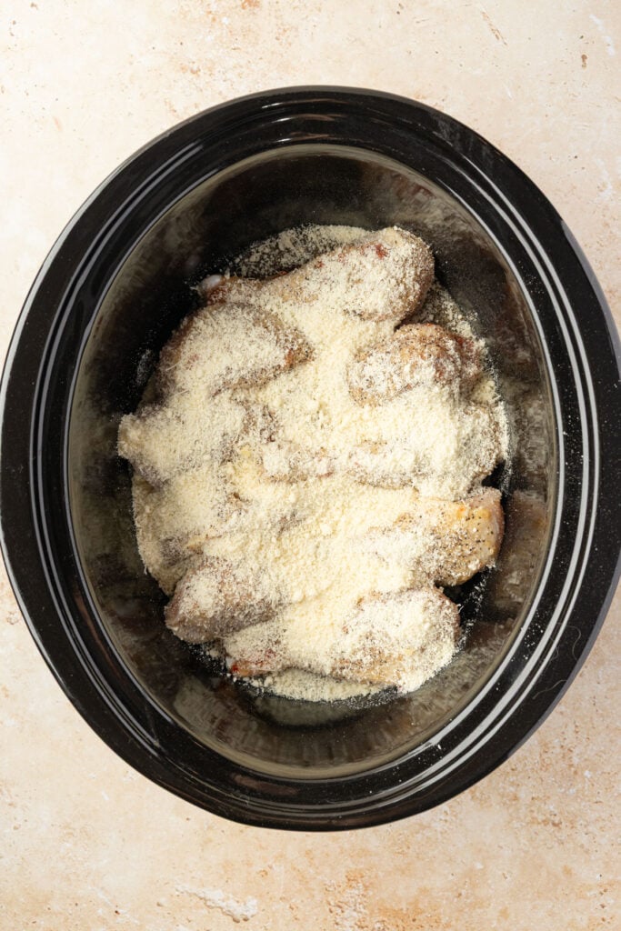 Chicken drumsticks in a slow cooker covered with Parmesan cheese and sauce.