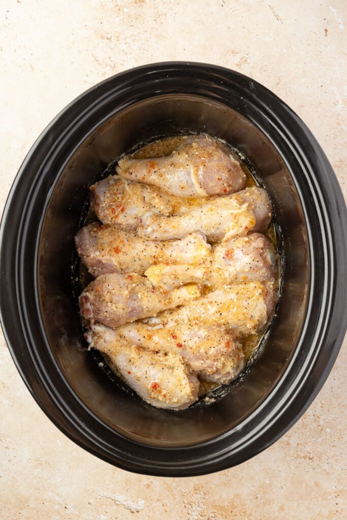 Raw chicken drumsticks in a slow cooker covered in sauce blend.