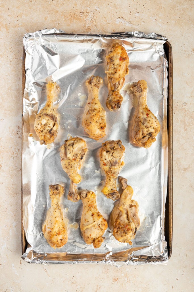 Chicken drumsticks on a sheet pan lined with aluminum foil.