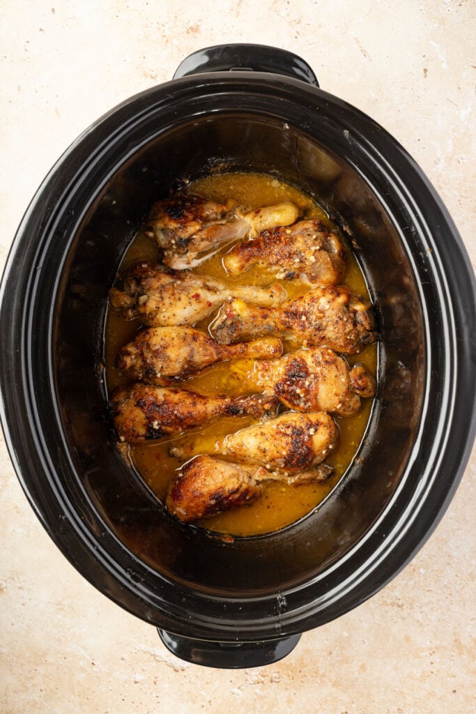 Slow cooker filled with finished slow cooker, chicken drumsticks.