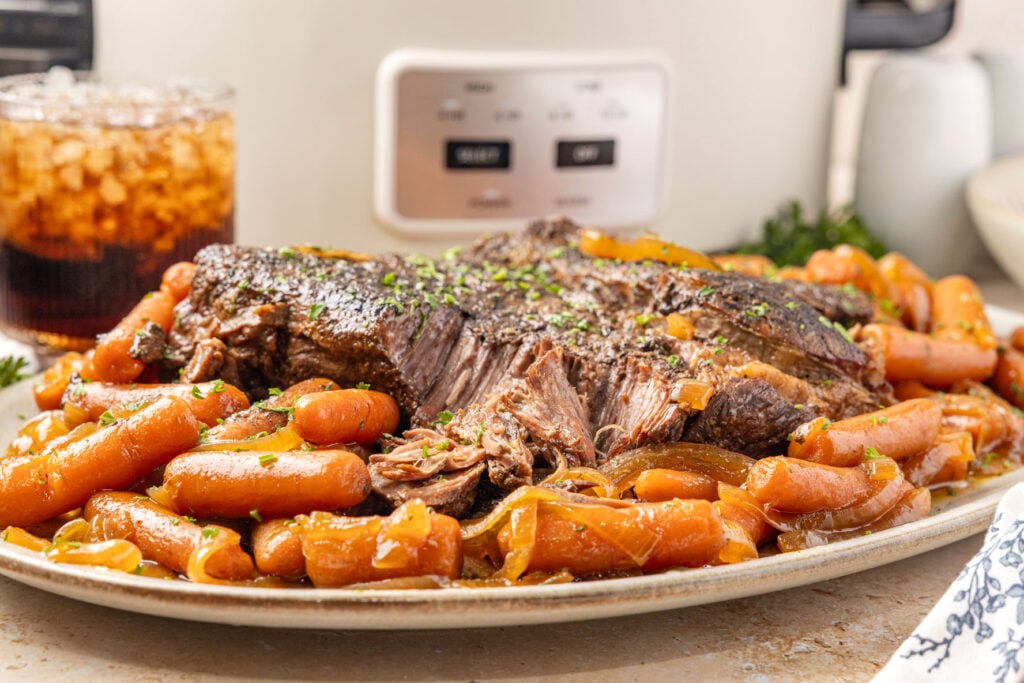 Slow Cooker Chuck Roast plated on a platter with the baby carrots surrounding it.