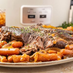 Slow Cooker Chuck Roast plated on a platter with the baby carrots surrounding it.