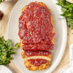 Thanksgiving meatloaf on a platter sliced with fresh herbs around it.