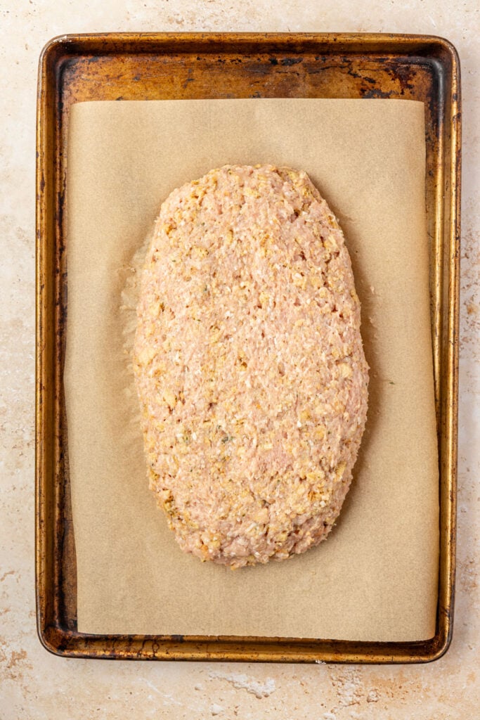 Raw turkey meatloaf on a sheet pan with parchment paper.