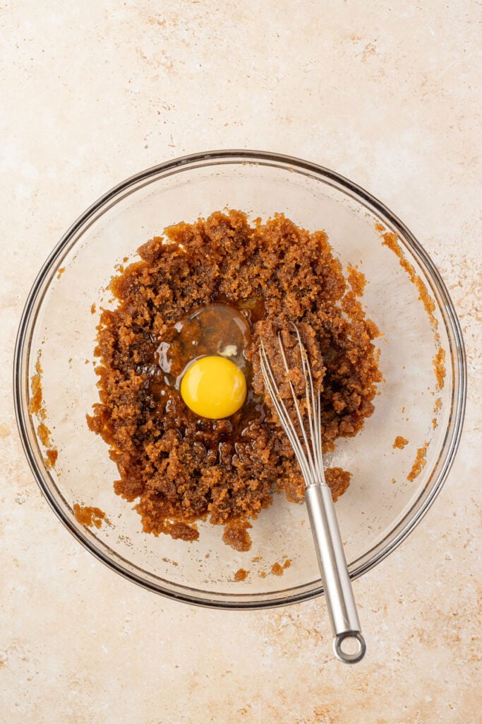 Brown sugar and butter, with an egg in a mixing bowl in a whisk.