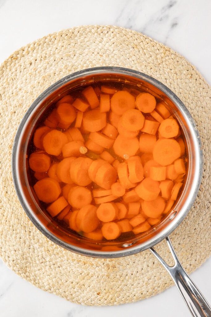 Sliced carrots boiling in water in a saucepan before being coated in brown sugar glaze.