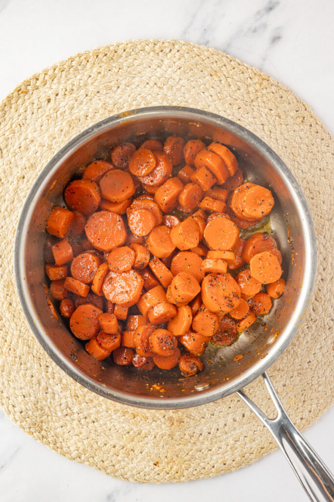 Sliced carrots coated in a buttery brown sugar glaze inside a saucepan after cooking.