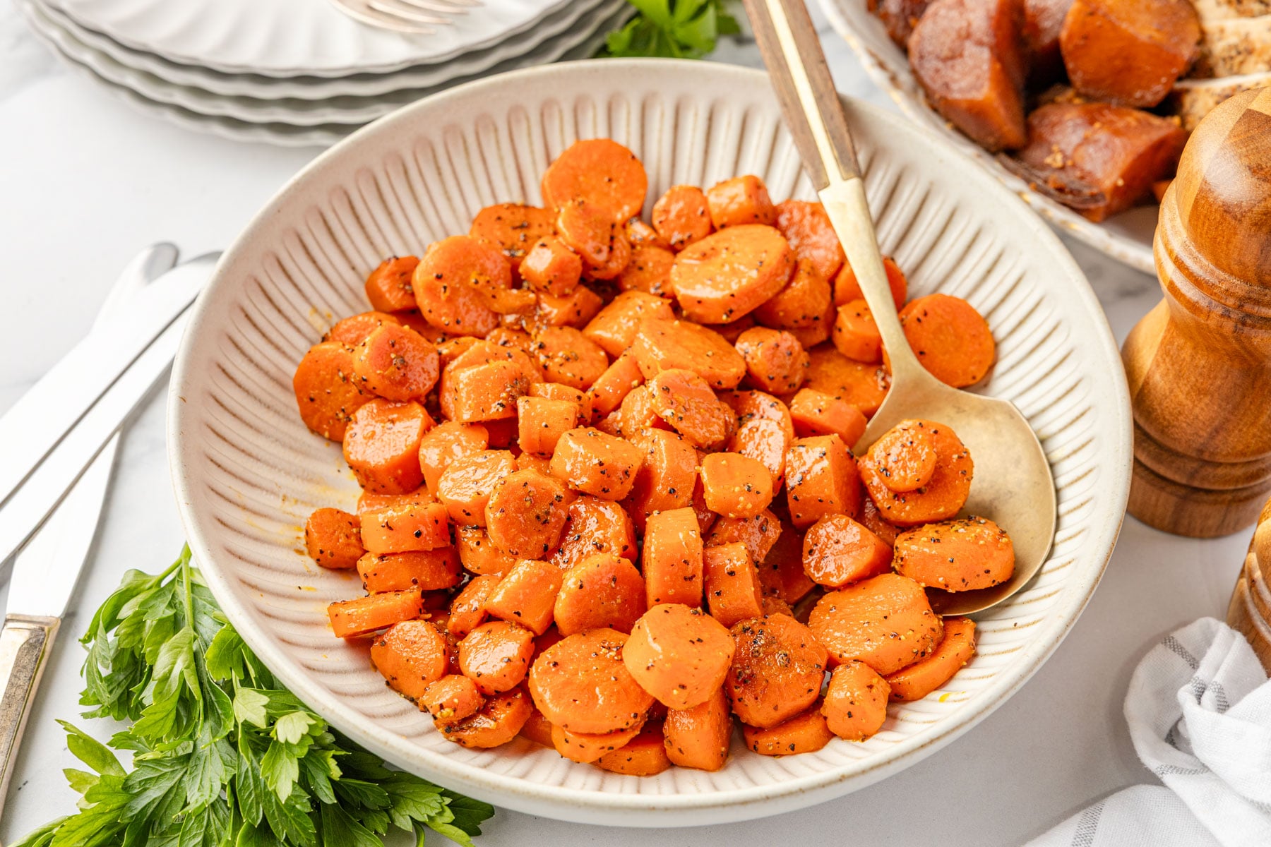 Overhead view of Brown Sugar Glazed Carrots in a white serving bowl with a wooden spoon.