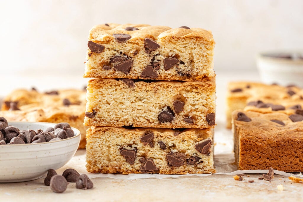 Cake Mix Cookie Bars stacked up on a marble background with a small bowls of chocolate chips.