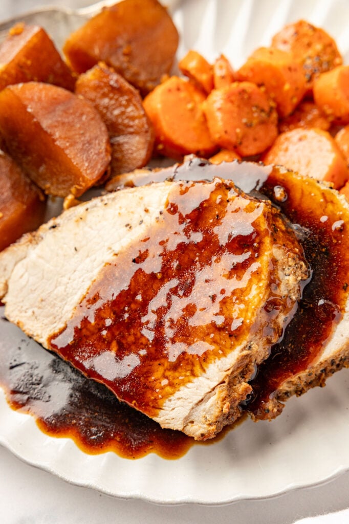 Close-up of a slice of Roasted Pork Loin topped with rich brown gravy and served with potatoes and carrots.