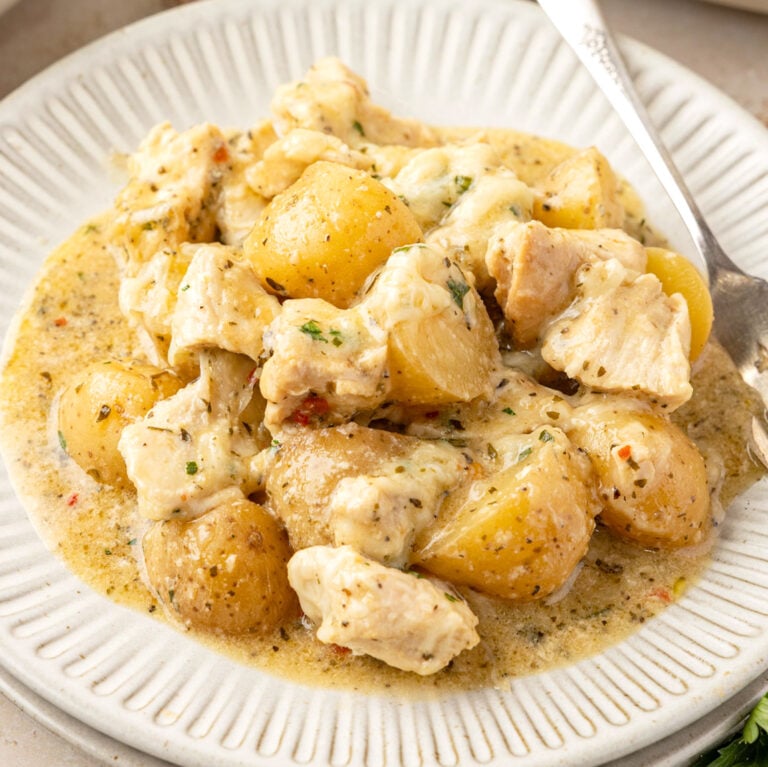 Plated Slow Cooker Garlic Parmesan Chicken And Potatoes with crockpot in the background.
