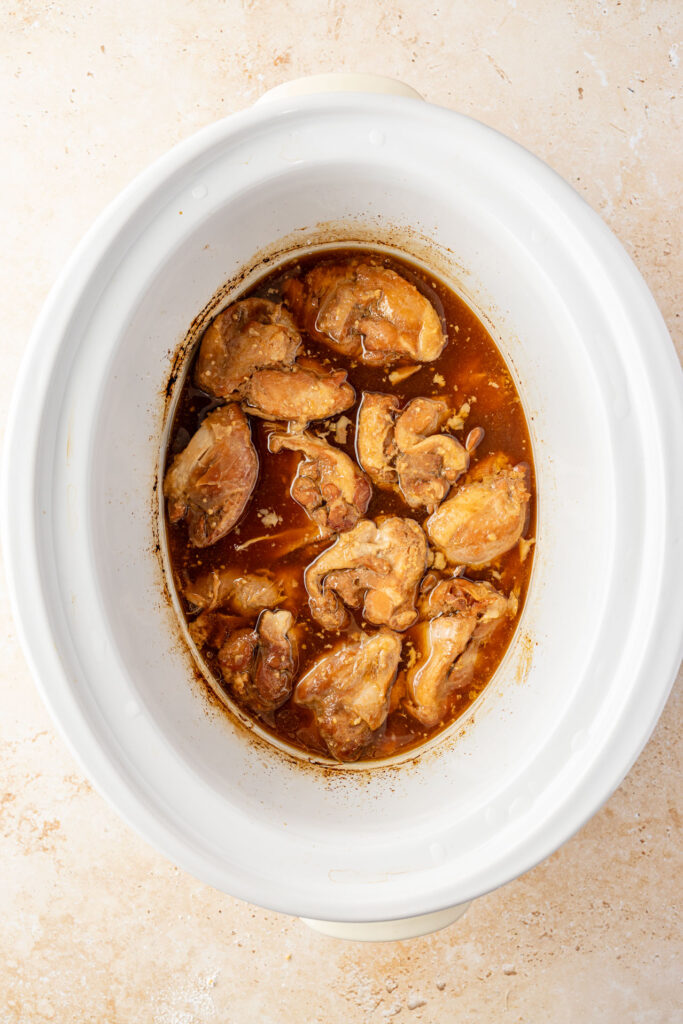 Boneless chicken thighs simmering in homemade teriyaki sauce inside a slow cooker.