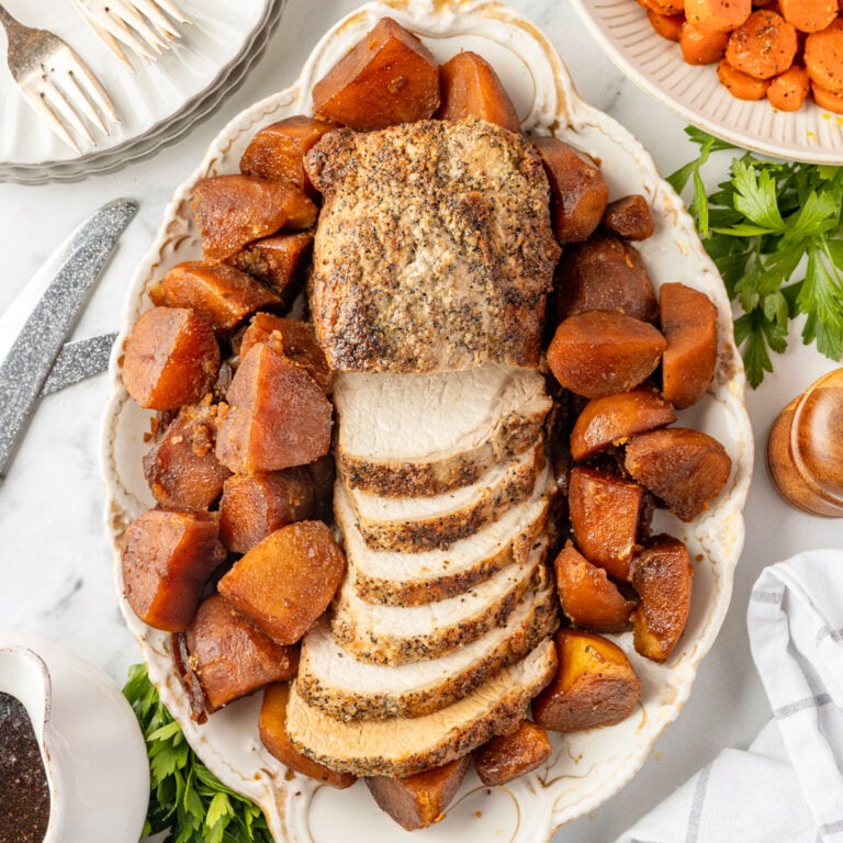 Overhead view of sliced Roasted Pork Loin surrounded by brown potatoes and carrots on a serving platter.